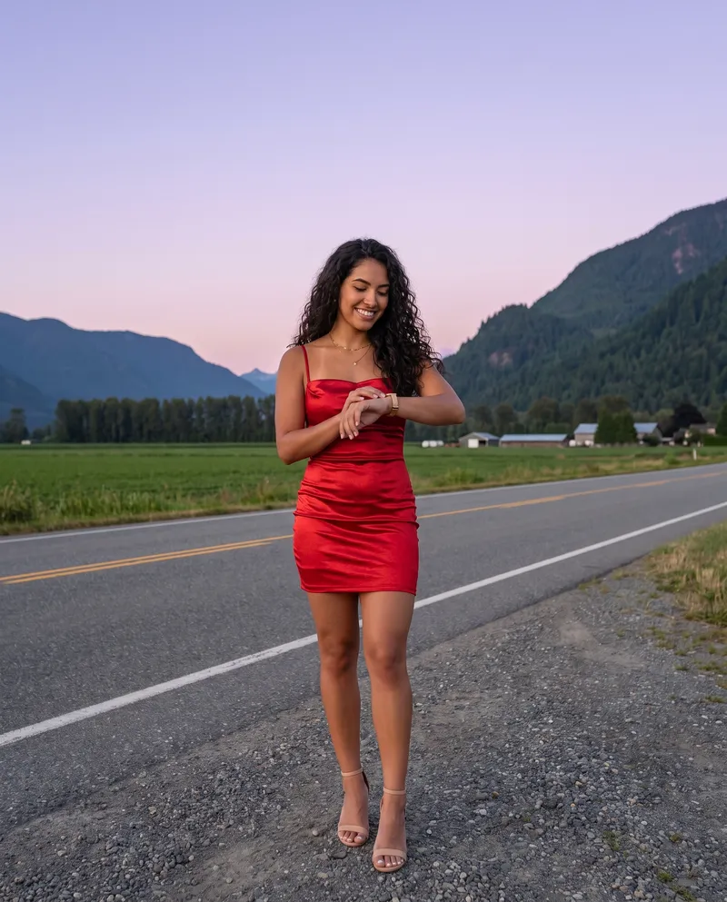 Generated picture of the same character on the shoulder of a quiet country road in a green farming valley at dusk, smiling at her wristwatch, with steep forested mountains and a violet sky behind.